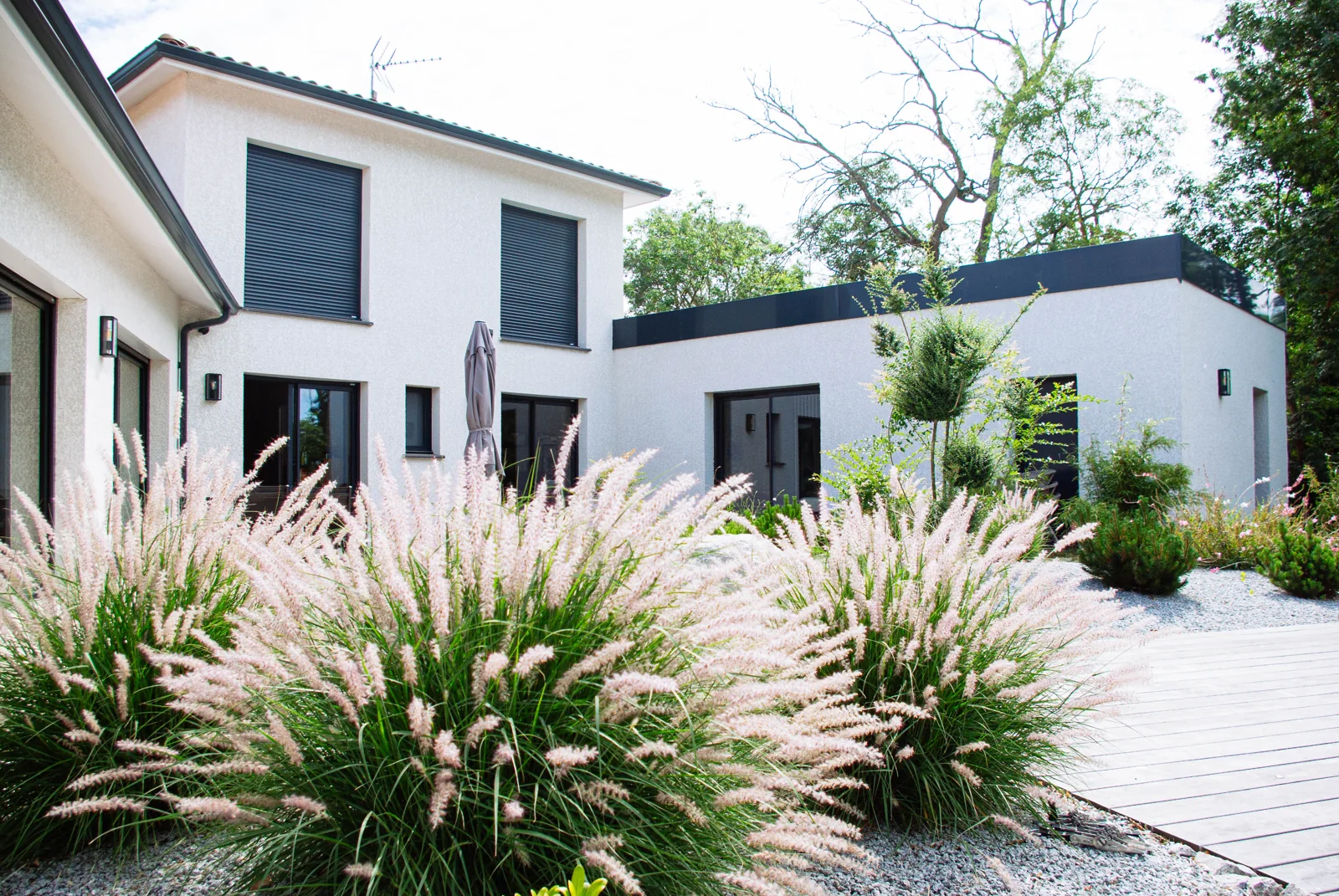 Maison CELIA ouverte sur une terrasse en bois et un jardin paysager.