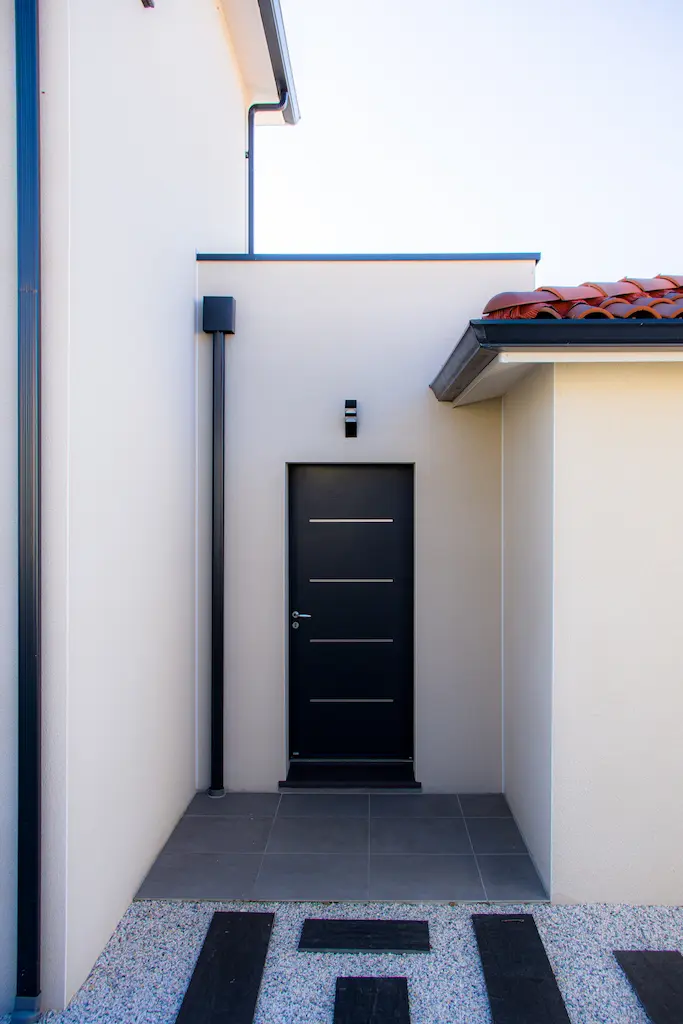 Entrée d’une maison contemporaine avec porte noire et toiture en tuiles réalisée par CELIA Création à Senouillac dans le Tarn.