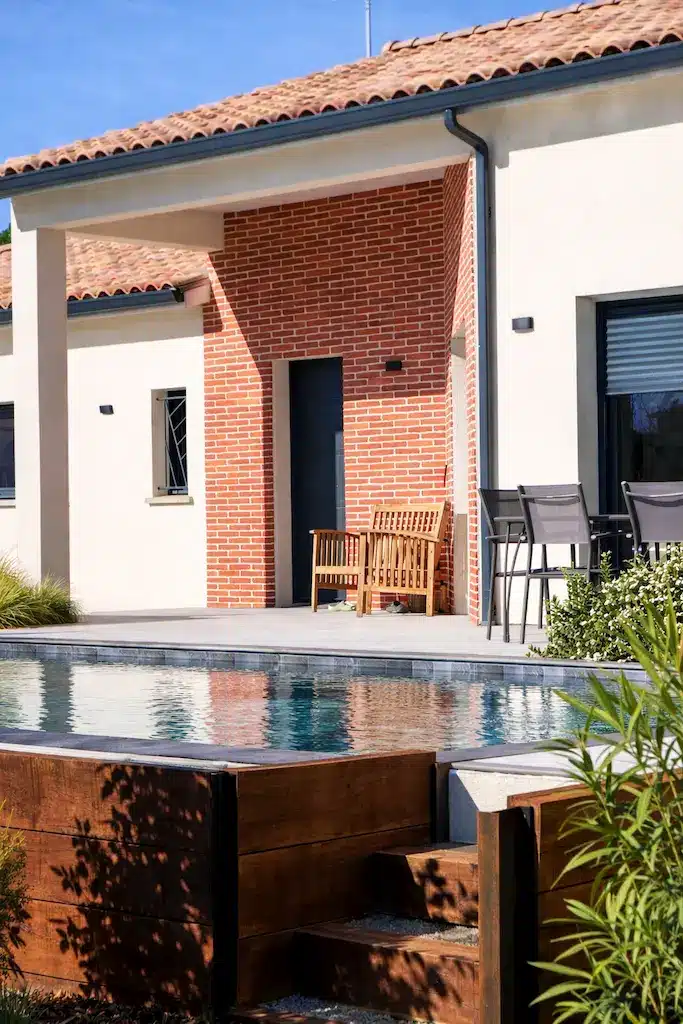 Terrasse avec piscine et façade en brique d’une maison moderne de plain-pied réalisée par CELIA Création à Rouffiac-Tolosan en Haute-Garonne